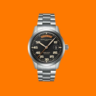 Maurice de Mauriac B&Auml;RN-DATE Uhr vor kr&auml;ftigem Orange-Hintergrund. Klare Linien, sportlich-elegantes Design und Schweizer Pr&auml;zision vereint in einem ikonischen Zeitmesser.
